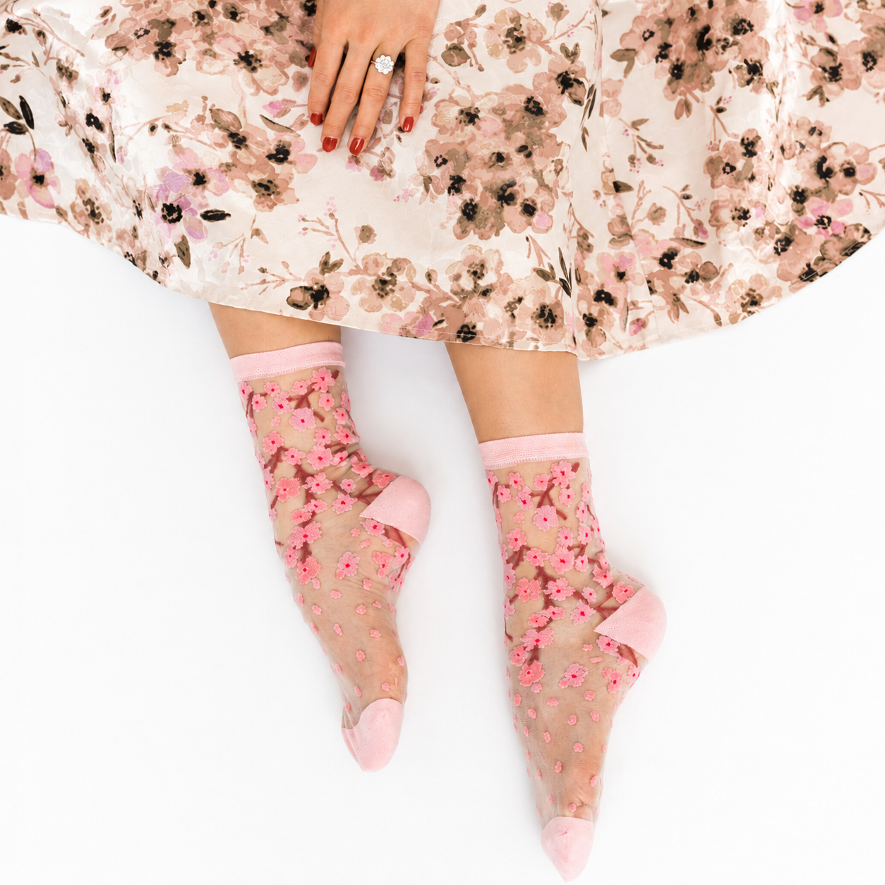 Person sitting on a white surface wearing a floral skirt and sheer pink cherry blossom socks.