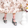 Legs wearing sheer cherry blossom socks and chunky floral platform heels next to a white vase.
