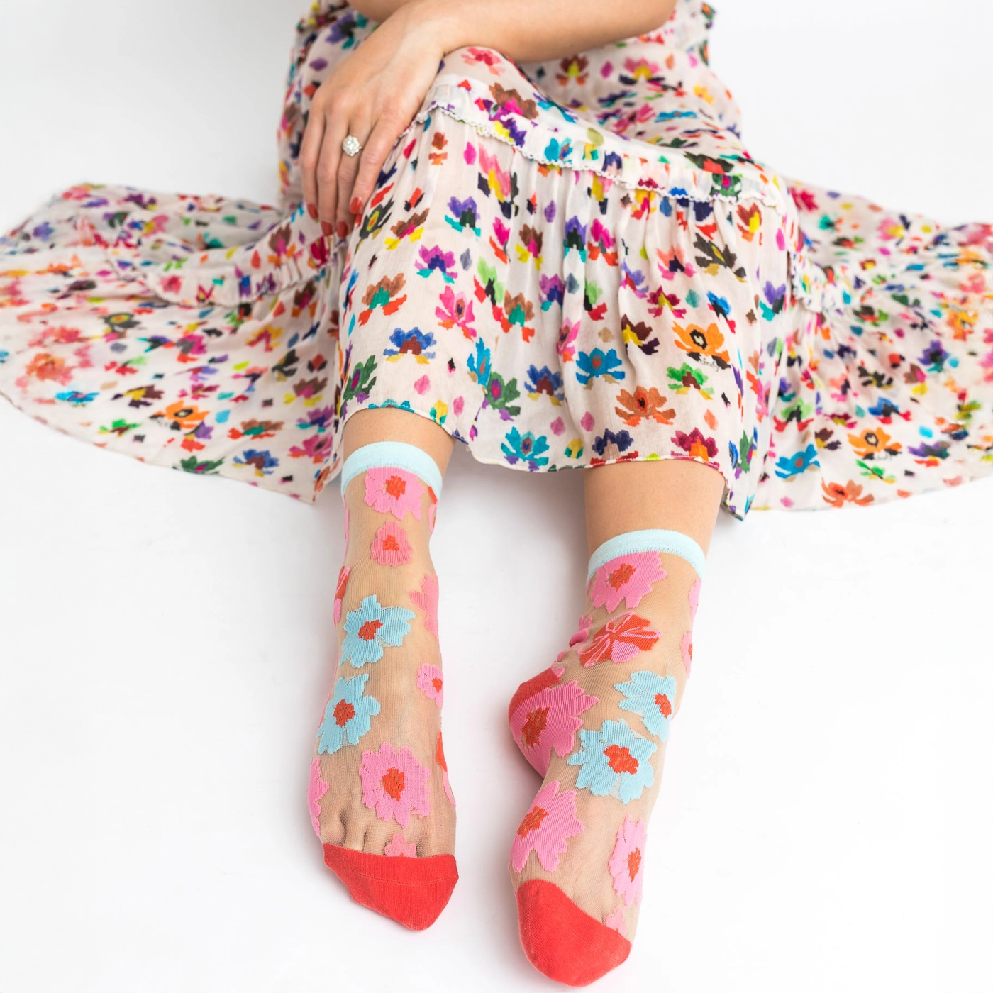 Person sitting in a floral dress wearing sheer socks with pink and blue flowers, with skin visible through the mesh fabric.