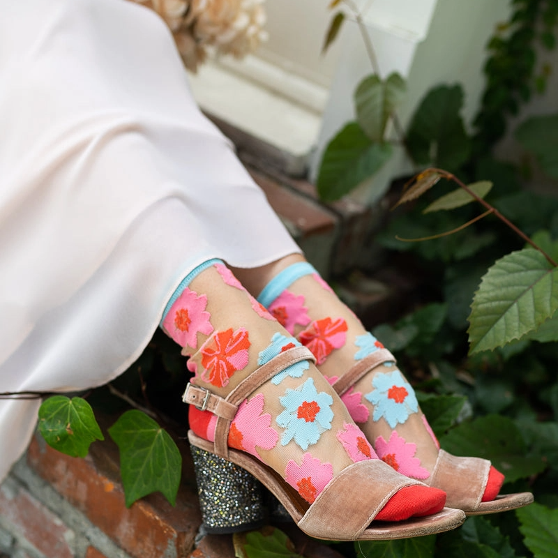 Close view of sheer floral socks worn with strappy velvet heels, showing red solid toes and light blue cuffs on the wearer.