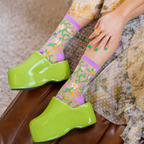 Close-up of sheer floral socks showing green vine hearts and colorful flowers worn with yellow crystal-embellished heels.