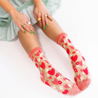 Person sitting in a light green dress wearing sheer strawberry socks, with hands resting on their knees.