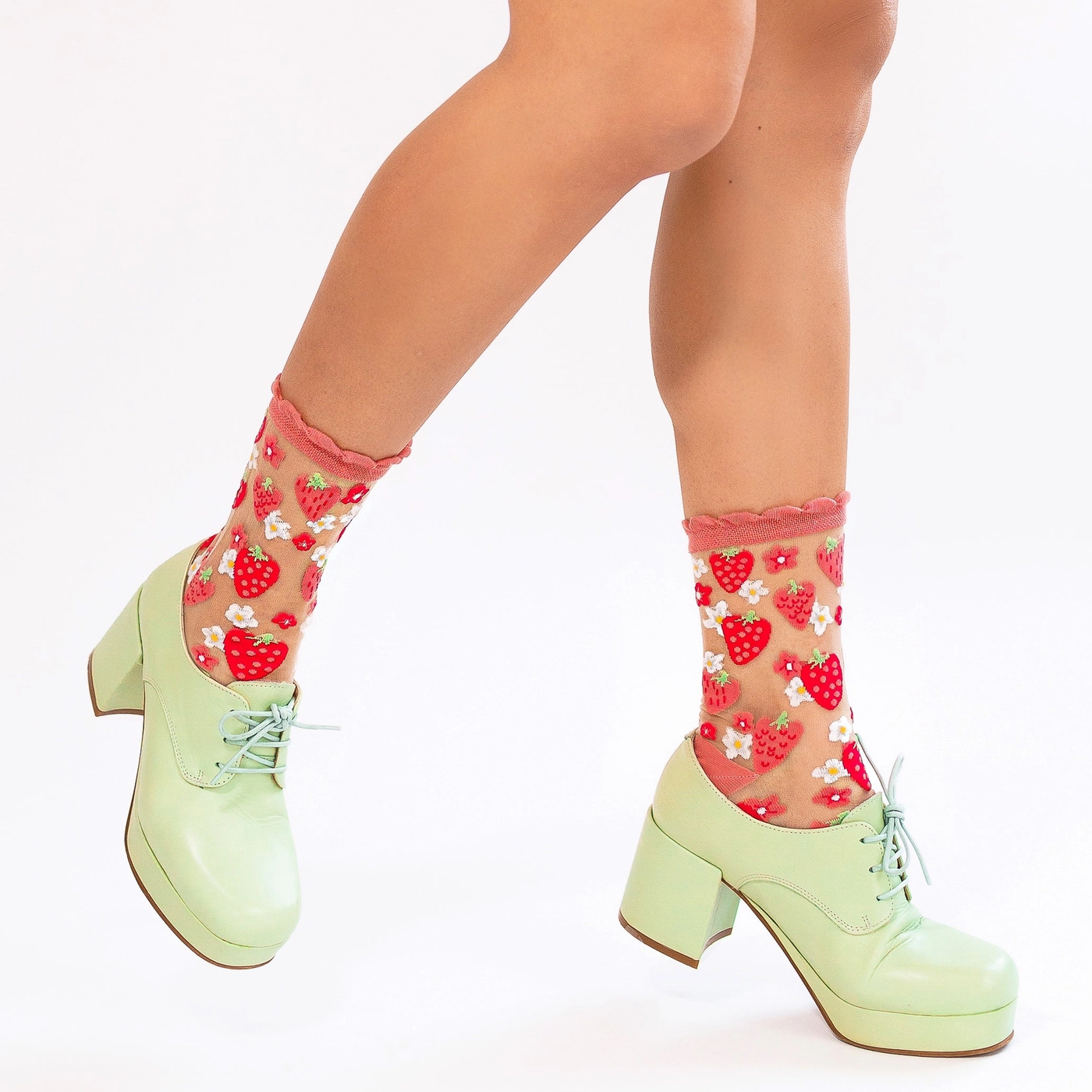 Legs walking in chunky pastel green oxfords, showing off sheer socks with a red strawberry and white daisy pattern.