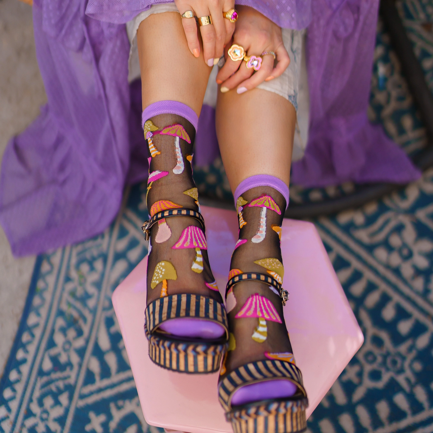 Feet on a pink stool wearing sheer mushroom socks and striped platform sandals.