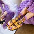 Person wearing sheer mushroom socks with yellow buckle sandals next to a white wavy mirror.
