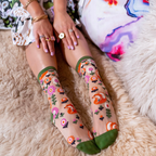 Legs on a fluffy rug wearing sheer fox socks, hands resting on knees with rings and a floral dress.