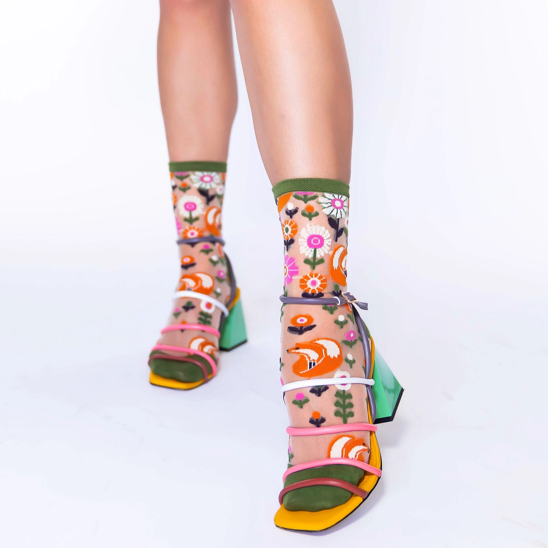 Close-up of translucent socks showing bright orange curled-up foxes and pink flowers against sheer mesh fabric.