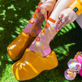 Close up of legs wearing sheer smiley daisy socks and chunky yellow clog shoes, standing on bright green artificial grass.
