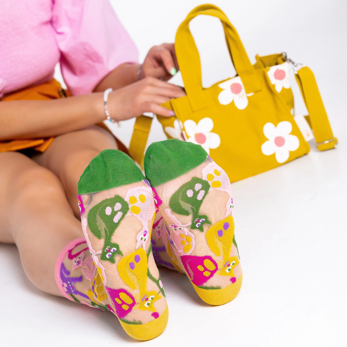 Bottom view of sheer cat socks showing solid green toes and yellow heels, with a yellow floral bag in the background.