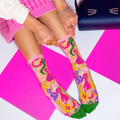 Person in a pink skirt pulling up the pink cuff of a sheer cat sock, with a dark blue cat-shaped purse nearby.