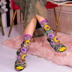 Person wearing sheer sunflower socks styled with green and gold open-toe heels, sitting with feet on a pink fluffy rug.