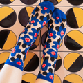 Point of view looking down at feet wearing sheer blue floral socks, standing against geometric black and yellow tiles.