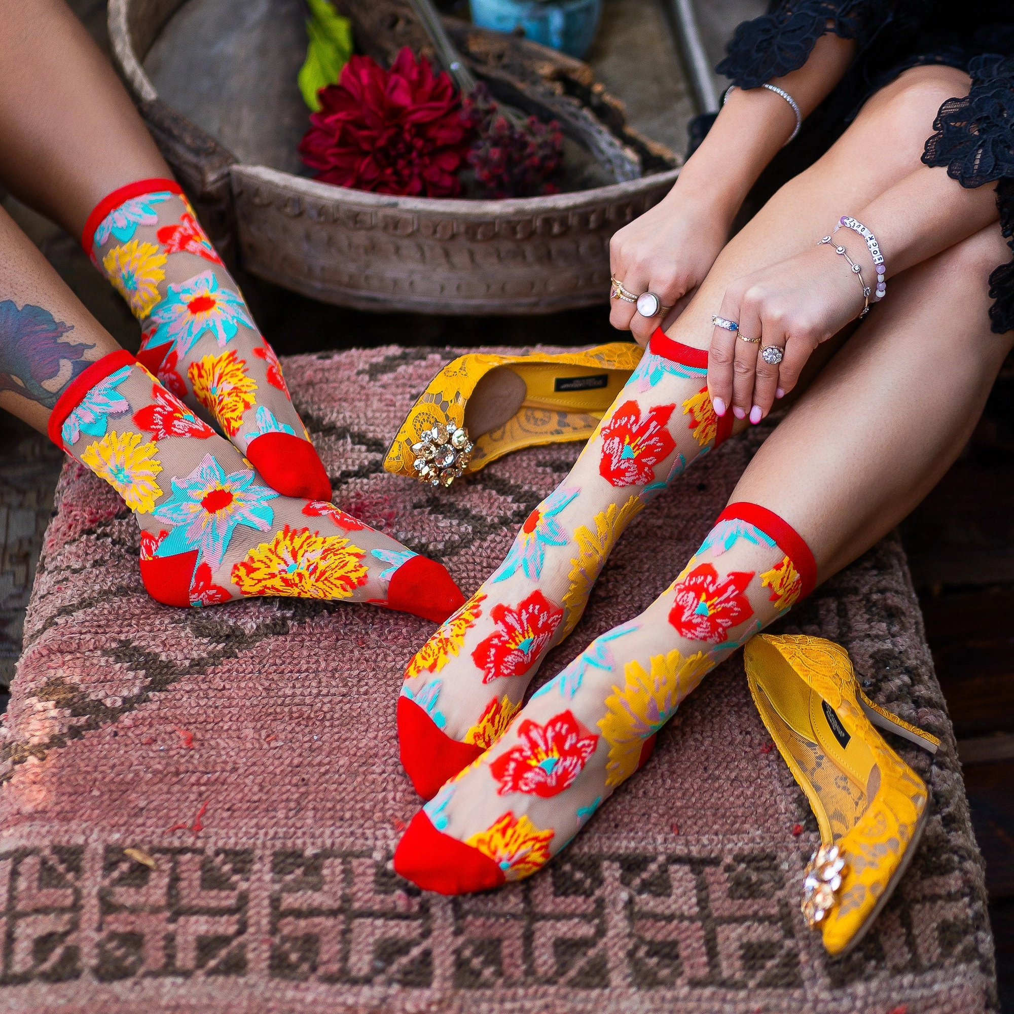 Sheer socks with yellow, teal, orange, and red flowers against a black background with solid red cuffs and toes.