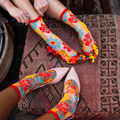 Two people wearing sheer floral socks and resting their feet on a patterned cushion next to yellow lace heels.