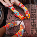 Two people wearing sheer floral socks and resting their feet on a patterned cushion next to yellow lace heels.