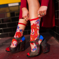 Person's legs crossed at the ankles wearing sheer horse socks and chunky sparkly high heels on a street with red lanterns.