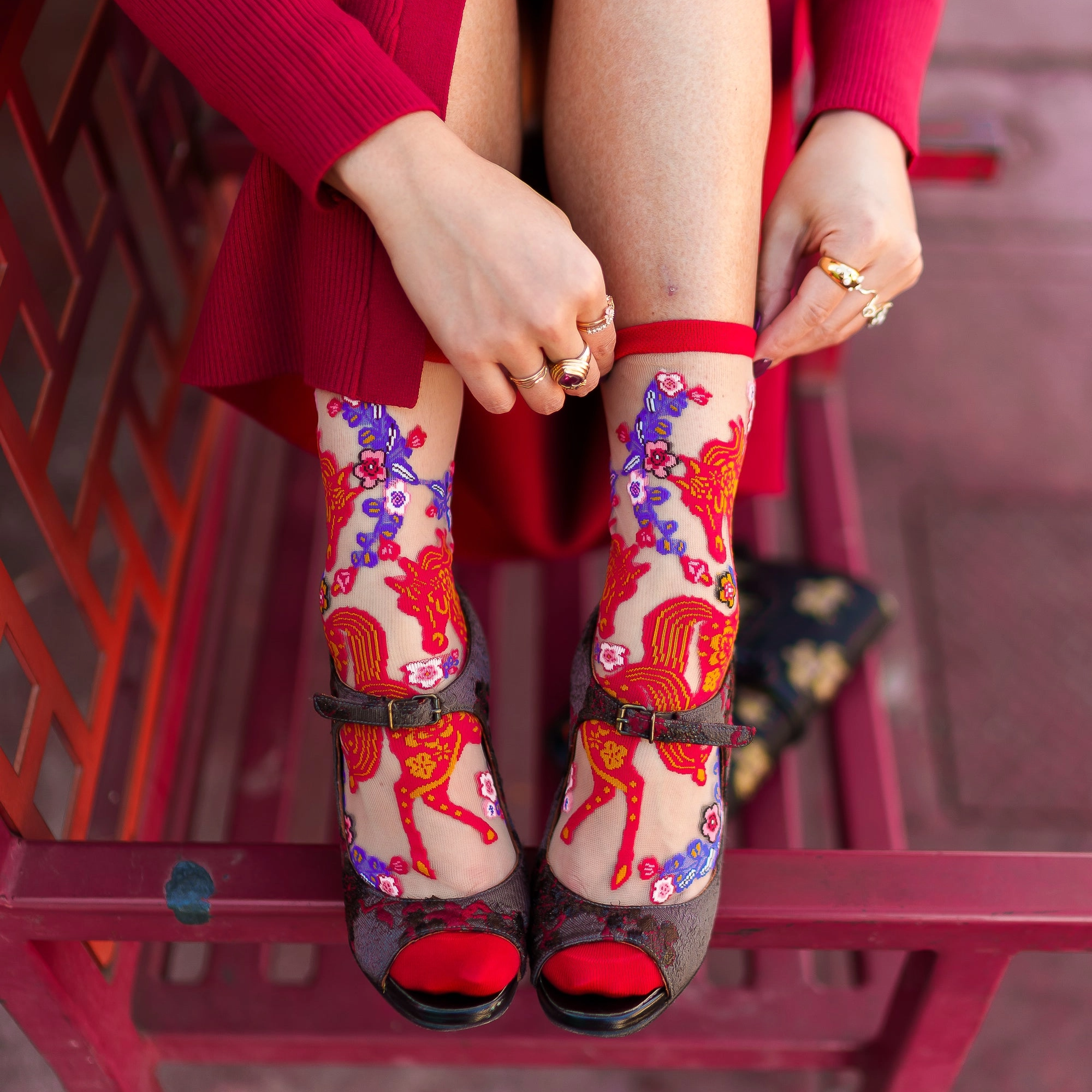 Side profile of legs wearing sheer horse socks and sparkly block heels, standing outdoors with a red structural background.