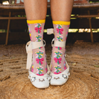 Close up of legs wearing sheer floral socks in white flat shoes with star details, standing on a woven circular rug.