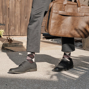 Close-up of Black Argyle dress socks with maroon and grey diamonds, paired with grey trousers, brown leather oxfords, and a tan leather briefcase. [lf]