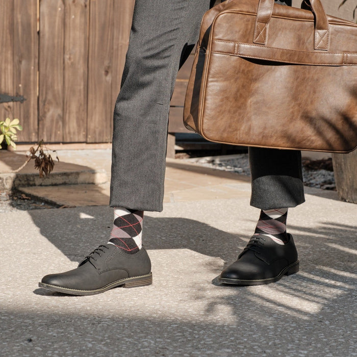 Close-up of Black Argyle dress socks with maroon and grey diamonds, paired with grey trousers, brown leather oxfords, and a tan leather briefcase. [lf]