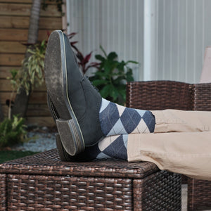 Close-up of Blue Argyle socks with grey and cream diamonds peeking above black leather boots, propped casually on a wicker ottoman with khaki pants. [lf]