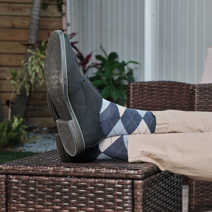 Close-up of Blue Argyle socks with grey and cream diamonds peeking above black leather boots, propped casually on a wicker ottoman with khaki pants. [lf]