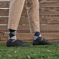A relaxed standing pose on grass showing Blue Argyle dress socks paired with khaki pants and black leather derby shoes against a wooden fence backdrop. [lf]