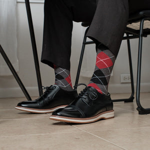 Charcoal Heather Argyle dress socks with bold red diamonds shown casually crossed at a desk, paired with grey dress slacks and black leather dress shoes. [lf]