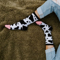 A close overhead view of bent knees in distressed jeans and MOOOO! in White socks resting on a brown sherpa throw. [lf]