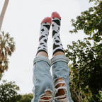 Legs kicked playfully into the air against a sky and palm tree backdrop showcase MOOOO! in White socks with pink toes. [lf]