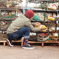 Wearer kneels at dockside crab traps tying gear, Seafood Platter socks peeking above black sneakers in profile view. [lf]