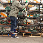 Standing among harbor crab gear and white buoys, the wearer shows off Seafood Platter socks beneath rolled jeans. [lf]
