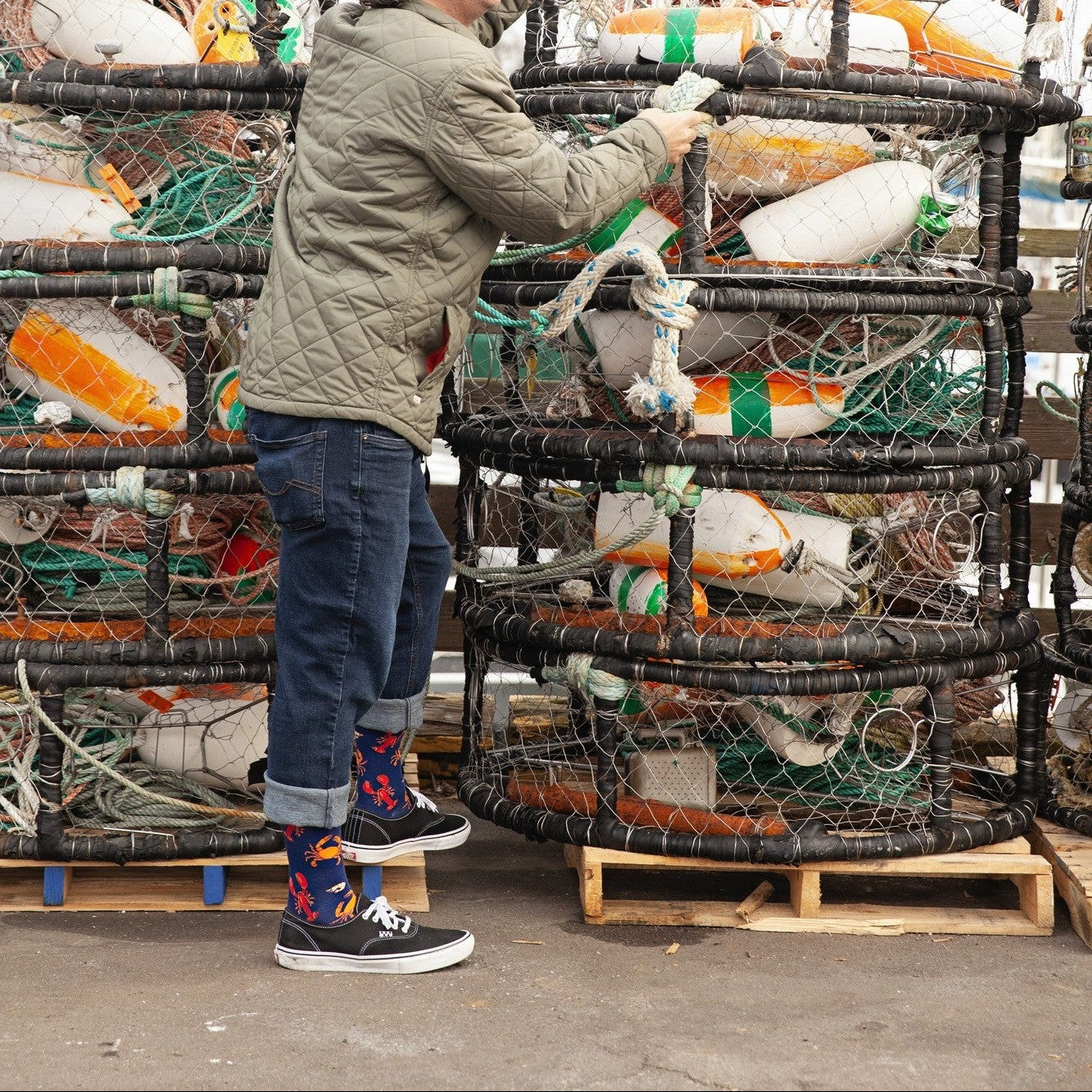 Standing among harbor crab gear and white buoys, the wearer shows off Seafood Platter socks beneath rolled jeans. [lf]