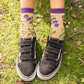 Feet planted on mossy ground show off Bunch of Blackberries Bamboo socks in Brown Heather, the purple ribbed cuffs and embroidered berry vines clearly visible above worn black Vans. [lf]