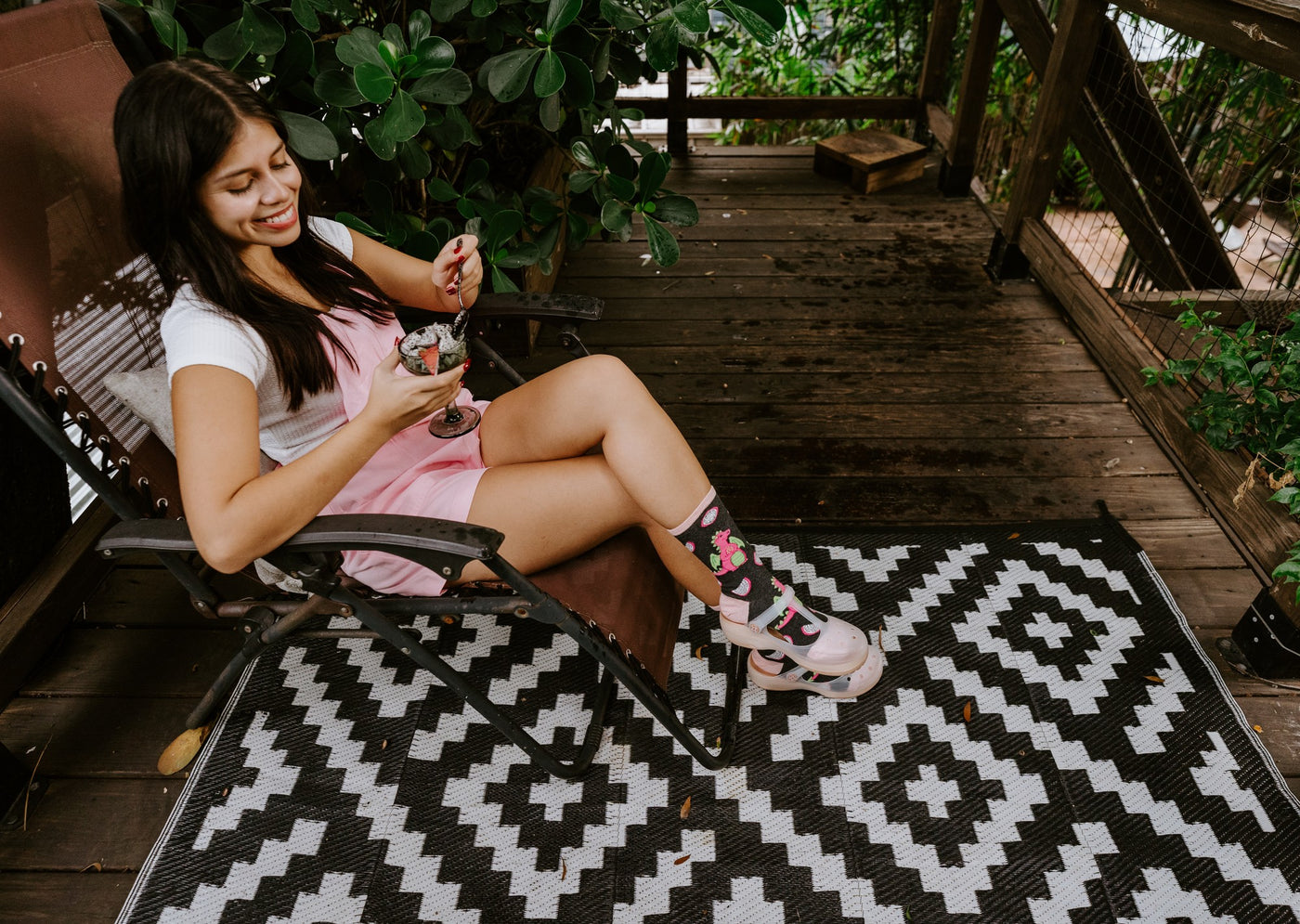 From across the diamond-patterned rug, a relaxed seated pose highlights Dragonfruit in Charcoal Heather socks while she stirs her drink with a spoon. [lf]