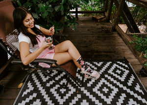 From across the diamond-patterned rug, a relaxed seated pose highlights Dragonfruit in Charcoal Heather socks while she stirs her drink with a spoon. [lf]