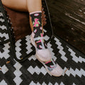 A vertical portrait of a woman reclining outdoors in a pink romper, sipping wine with crossed ankles in Dragonfruit in Charcoal Heather socks. [lf]