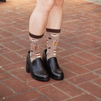 A woman stands on brick pavers holding a light-blue mug, posed full-length to show off Coffee, Coffee, Coffee Bamboo in Brown socks with black platform shoes. [lf]
