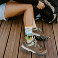 A close vertical view captures the full Yellowstone National Park in Yellow sock design, bison grazing under mountains and sun, as a hand reaches into a backpack nearby. [lf]