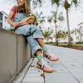 A vertical portrait of a woman seated on a wall holding a bouquet, her Cottage Garden in Green socks visible below cuffed overalls. [lf]