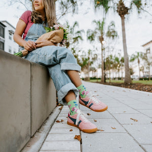 A vertical portrait of a woman seated on a wall holding a bouquet, her Cottage Garden in Green socks visible below cuffed overalls. [lf]