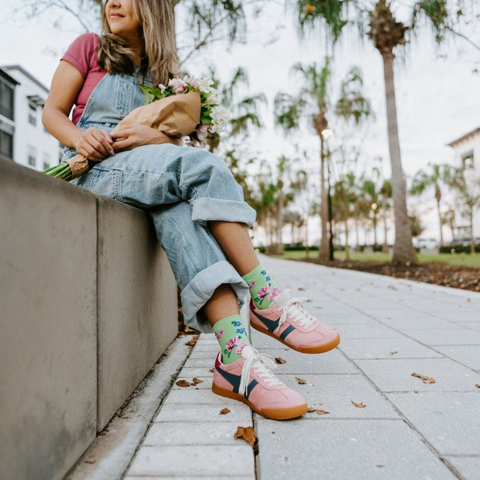 A vertical portrait of a woman seated on a wall holding a bouquet, her Cottage Garden in Green socks visible below cuffed overalls. [lf]