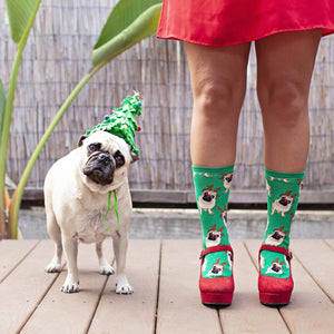 A close-up of Antler Pug socks featuring pug-with-antlers illustrations, on a person on a holiday rug. [lf]