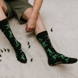 A pair of Army Men socks in BLACK stretched on a wood floor beside scattered green army figurines. [lf]