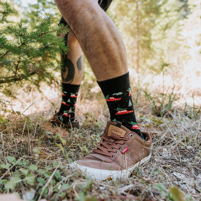 A holiday flatlay of Christmas Cars socks on a wood floor with a pine wreath, candy cane and gift tag. [lf]