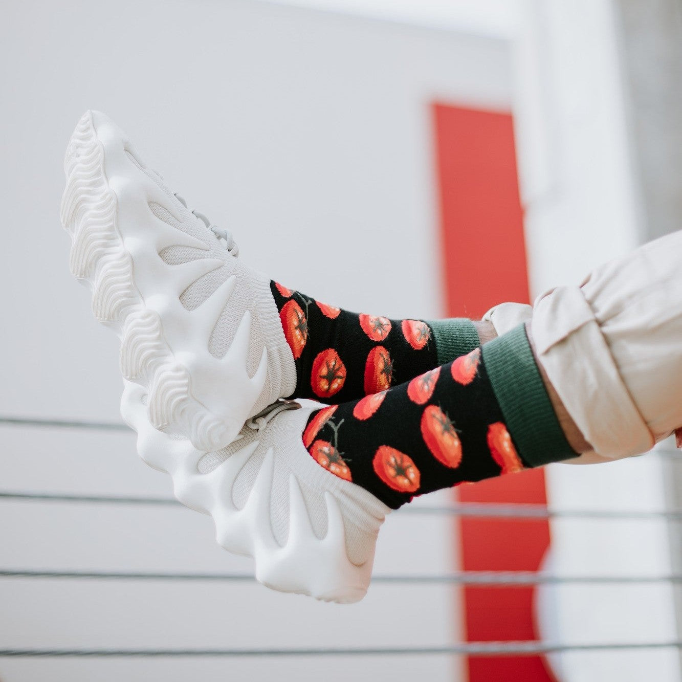 A close-up of Toe-May-Toes socks in Green featuring tomato illustrations, on a person in a kitchen garden. [lf]