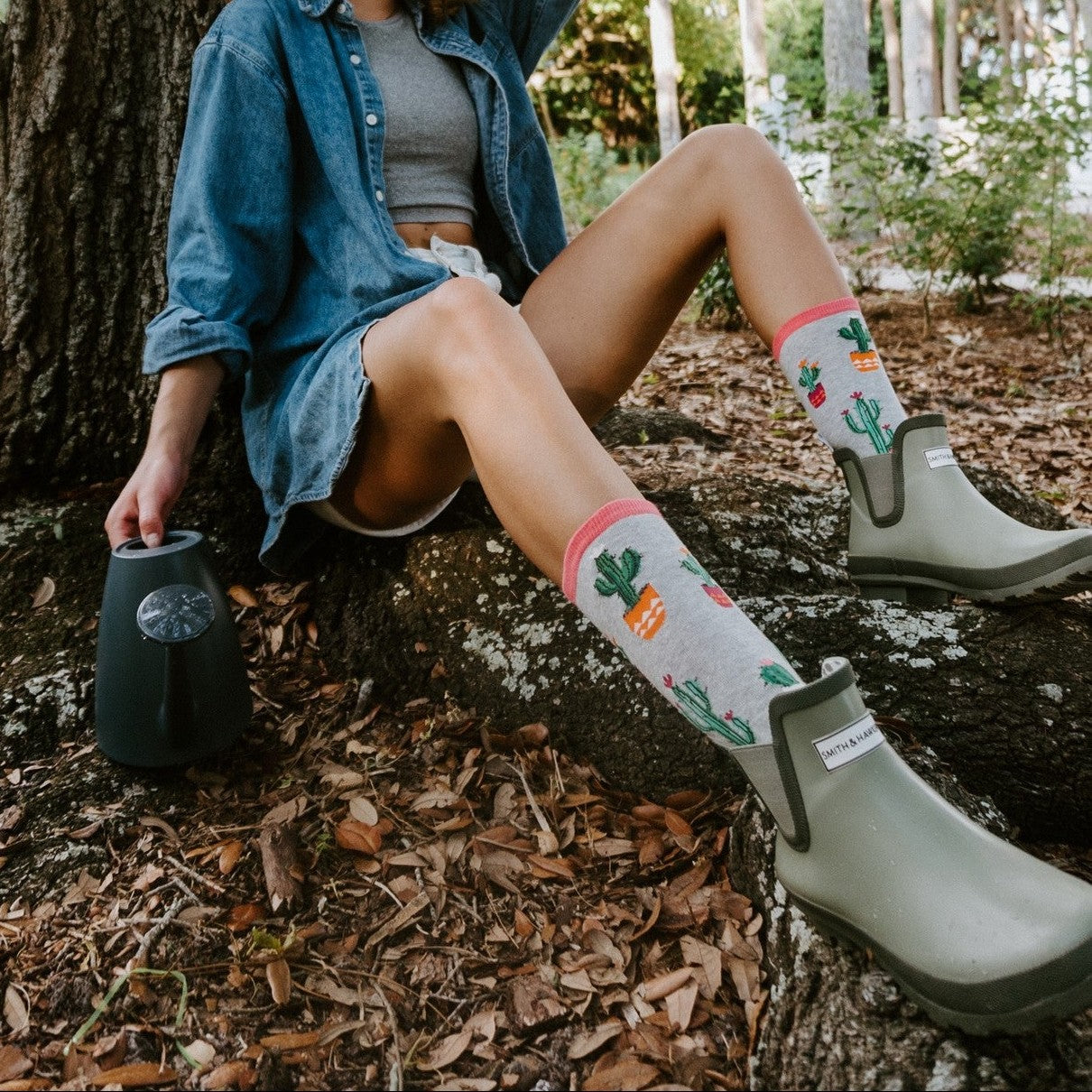 A friend in Court of Cactus socks in Light Gray Heather stands beside a tall saguaro at sunset, her socks vivid against the sand. [lf]