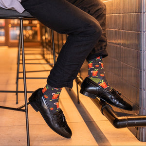 A close-up of Bloody Good Drink Bamboo socks in Charcoal Heather featuring Bloody Mary illustrations, on a person at a brunch table. [lf]