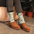 A friend reaches up to dust a tall philodendron, modeling Houseplants Bamboo socks in Blue with houseplant graphics. [lf]