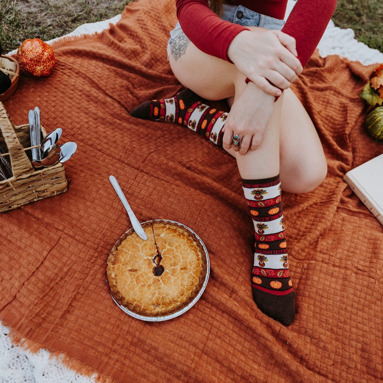 Two women in fall sweaters share pie at a Thanksgiving spread, modeling Gobble Gobble socks in Ivory Heather together. [lf]